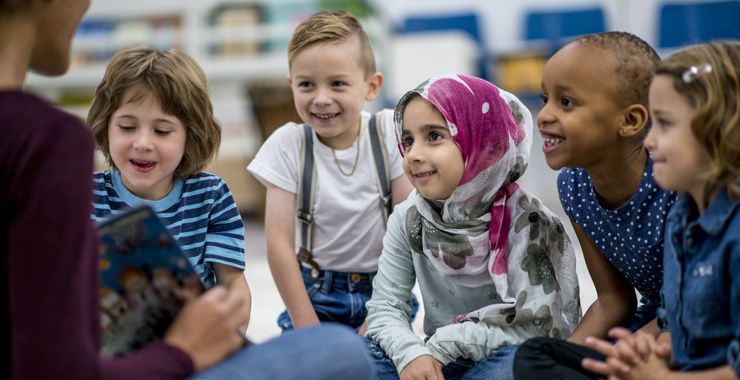 Young children listening to a teacher read a book in class