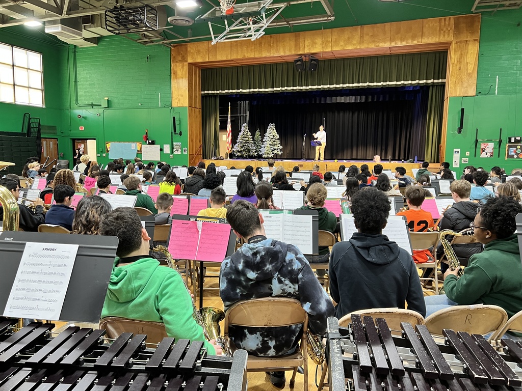 Students preparing to play their instruments while looking at a conductor on stage.